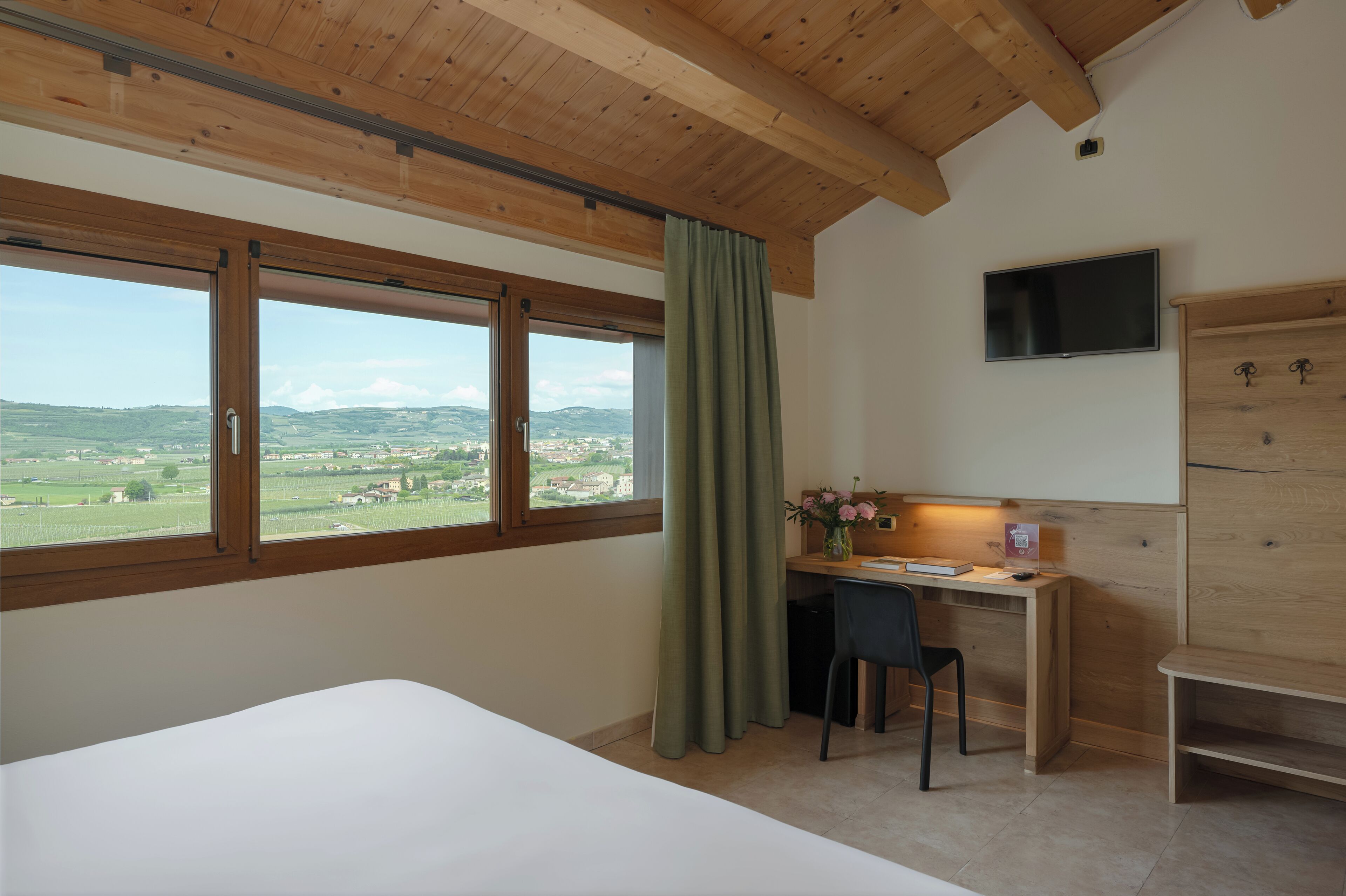 Ein Schlafzimmer mit großem Fenster, Schreibtisch, Stuhl, Fernseher und Kleiderschrank.