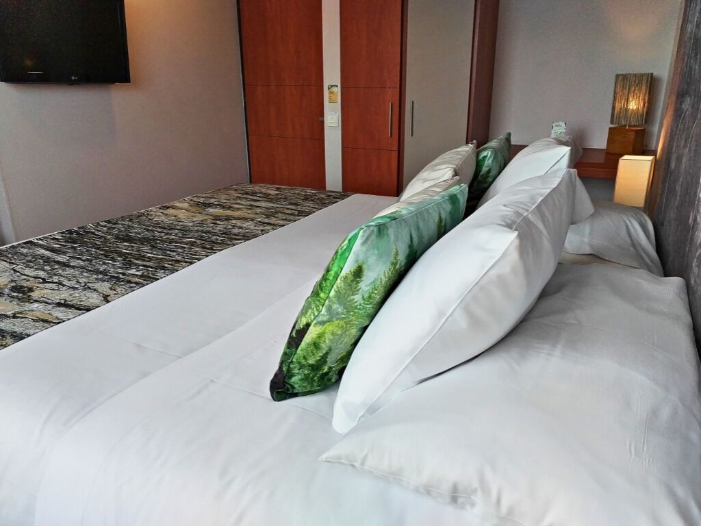 A hotel room with a bed, a flat-screen TV mounted on the wall, and a wooden wardrobe.