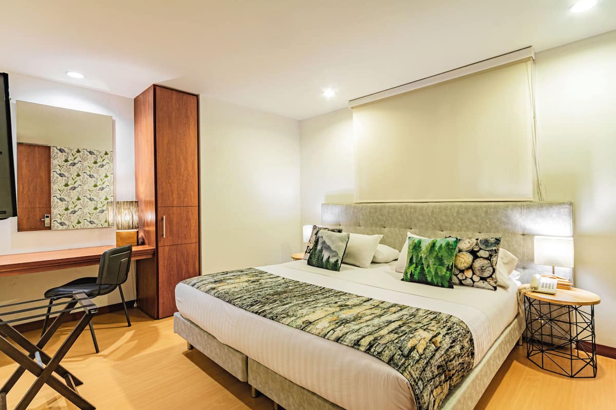 Une chambre d’hôtel avec un grand lit, un bureau avec une chaise, un miroir et une petite table ronde avec une lampe.