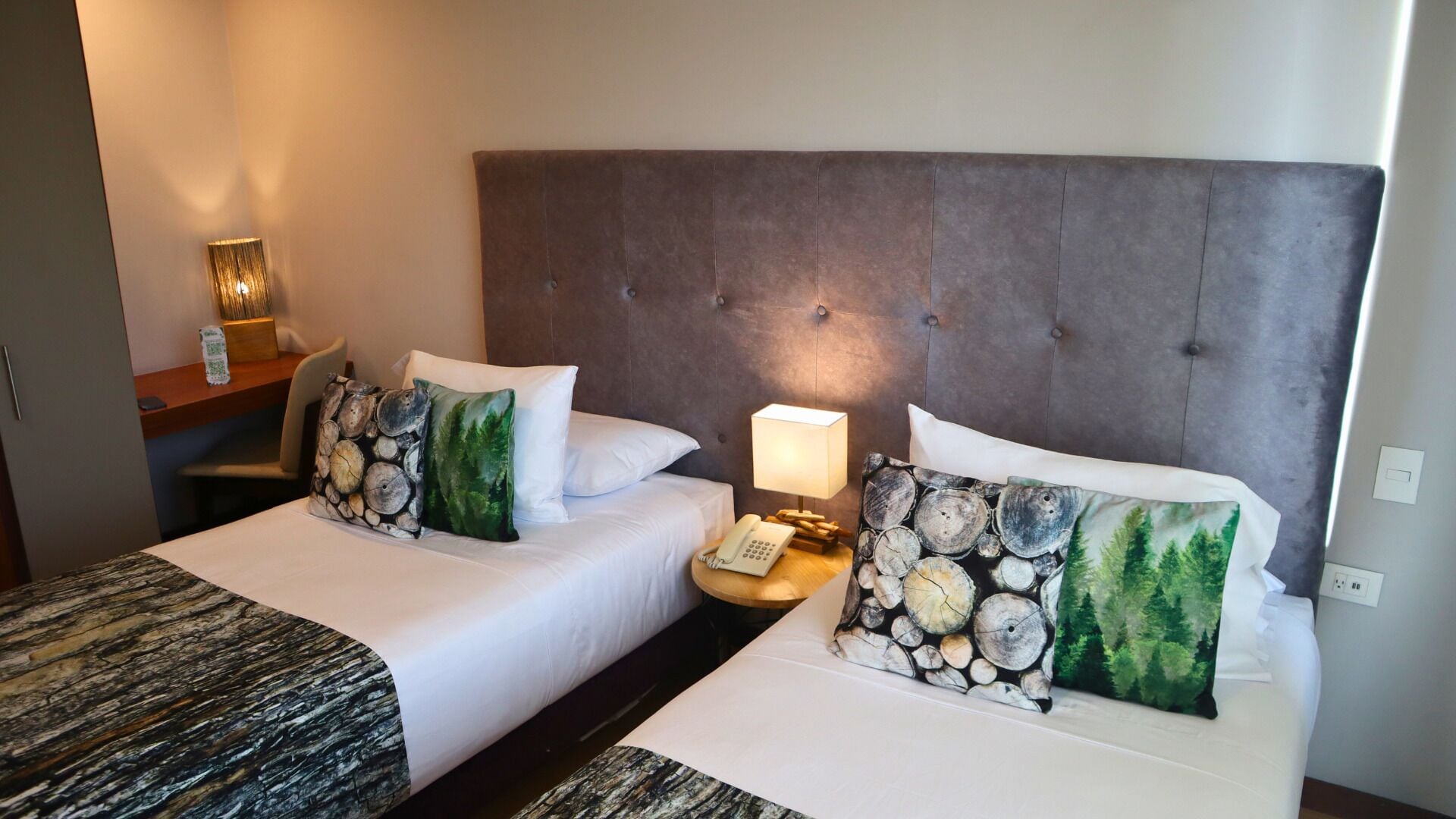 Une chambre d’hôtel avec deux lits, chacun doté d’une tête de lit, d’une table de chevet avec une lampe et de coussins décoratifs.