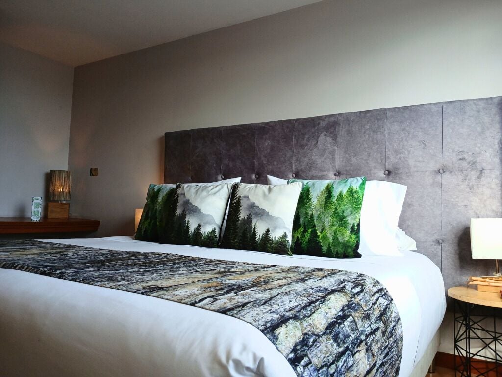 Una habitación de hotel con una cama grande, un cabecero gris y una mesita de noche con una lámpara.