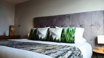 Una habitación de hotel con una cama grande, un cabecero gris y una mesita de noche con una lámpara.