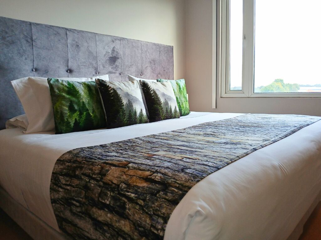 A bed with a grey headboard, white bedding, and a patterned throw blanket.