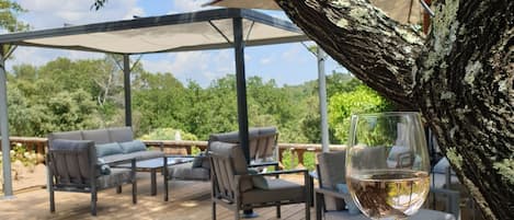 Un área de estar al aire libre con una mesa y sillas de vidrio, un porche cubierto y un árbol.