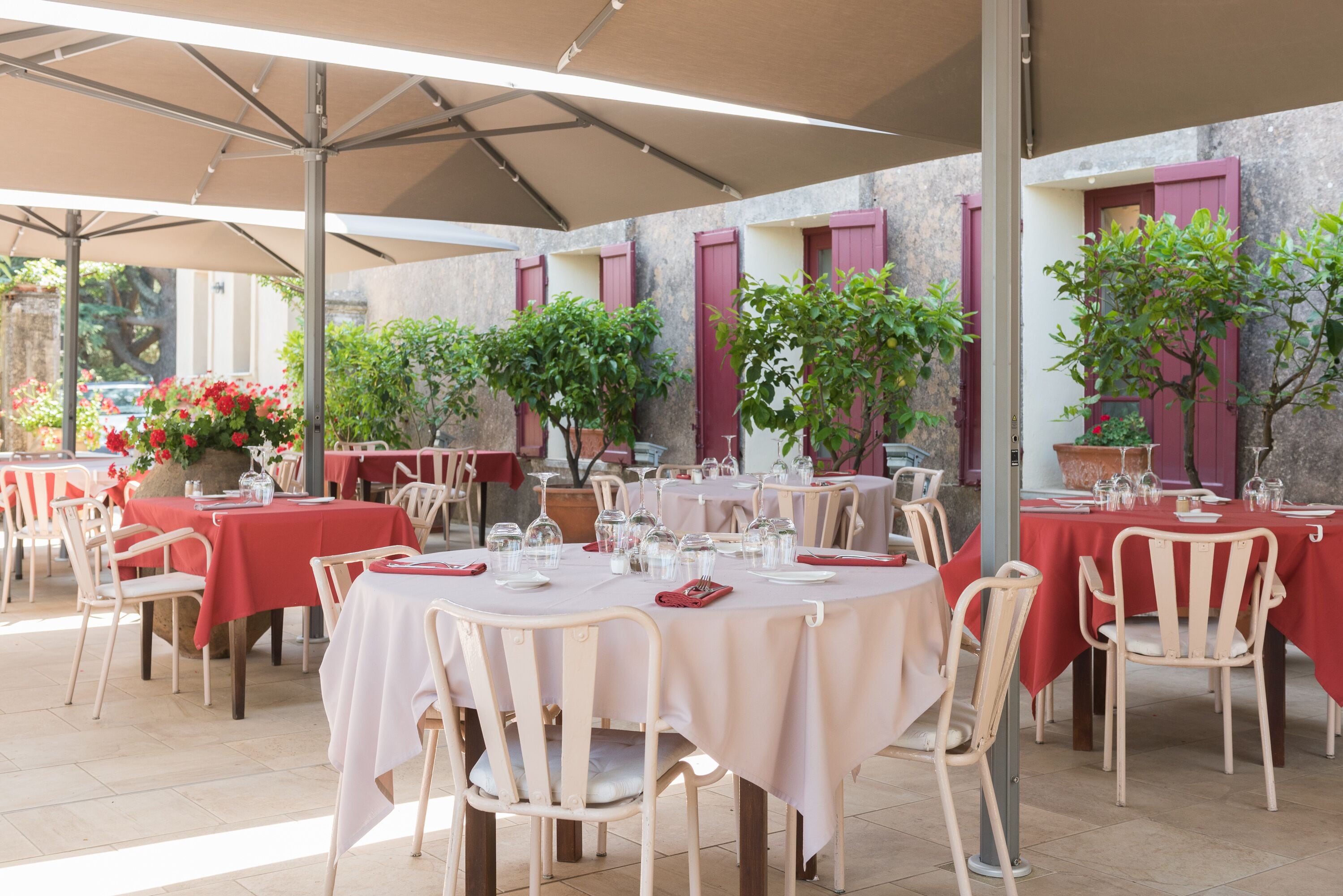 Un espace de restauration en plein air avec des tables rondes recouvertes de nappes blanches, entourées de chaises de couleur beige.