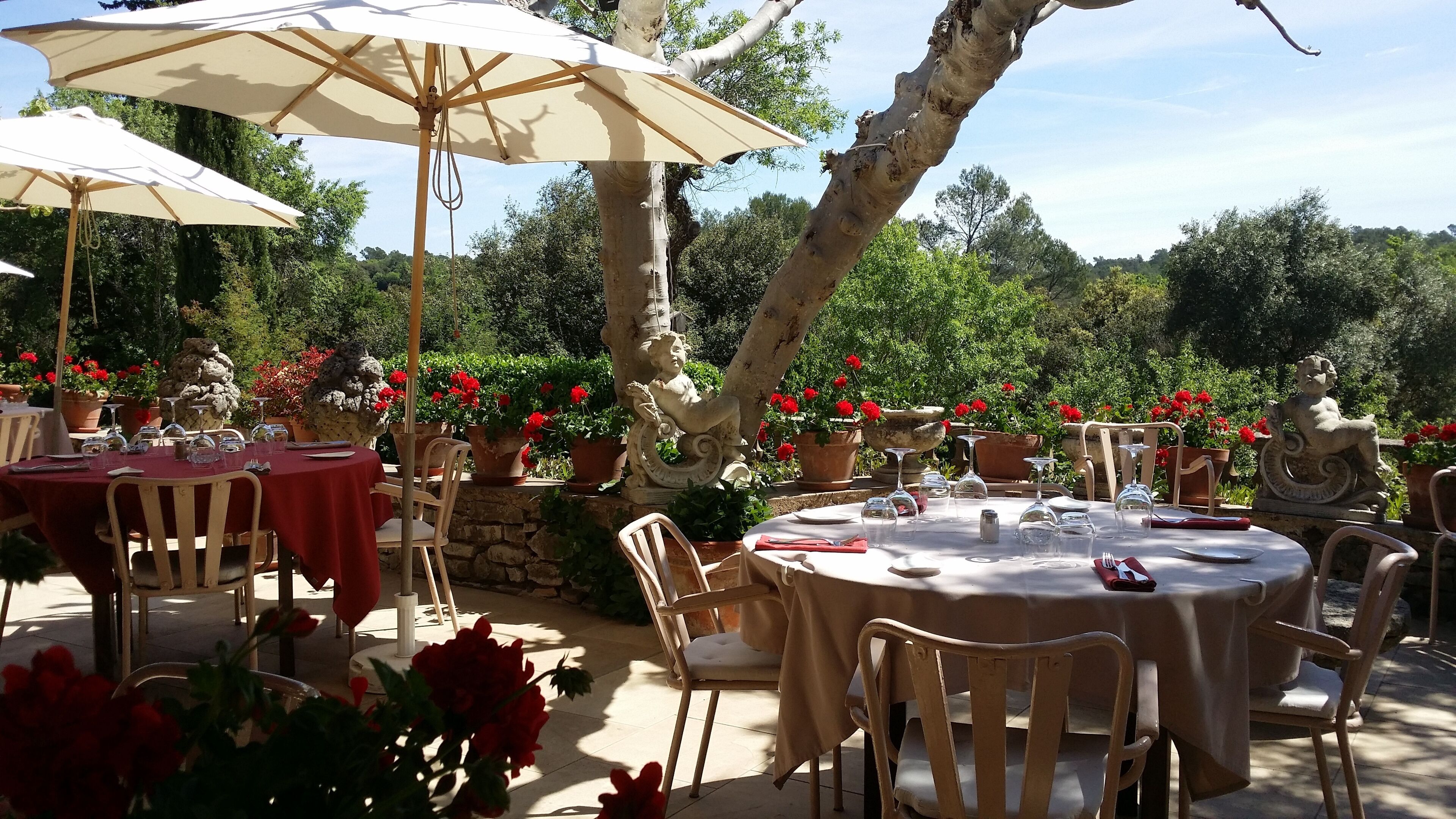 An outdoor dining area with round tables, chairs, and beige umbrellas.