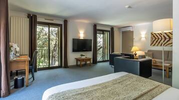 A hotel room with a bed, a desk, a chair, a sofa, a TV, and a window with curtains.