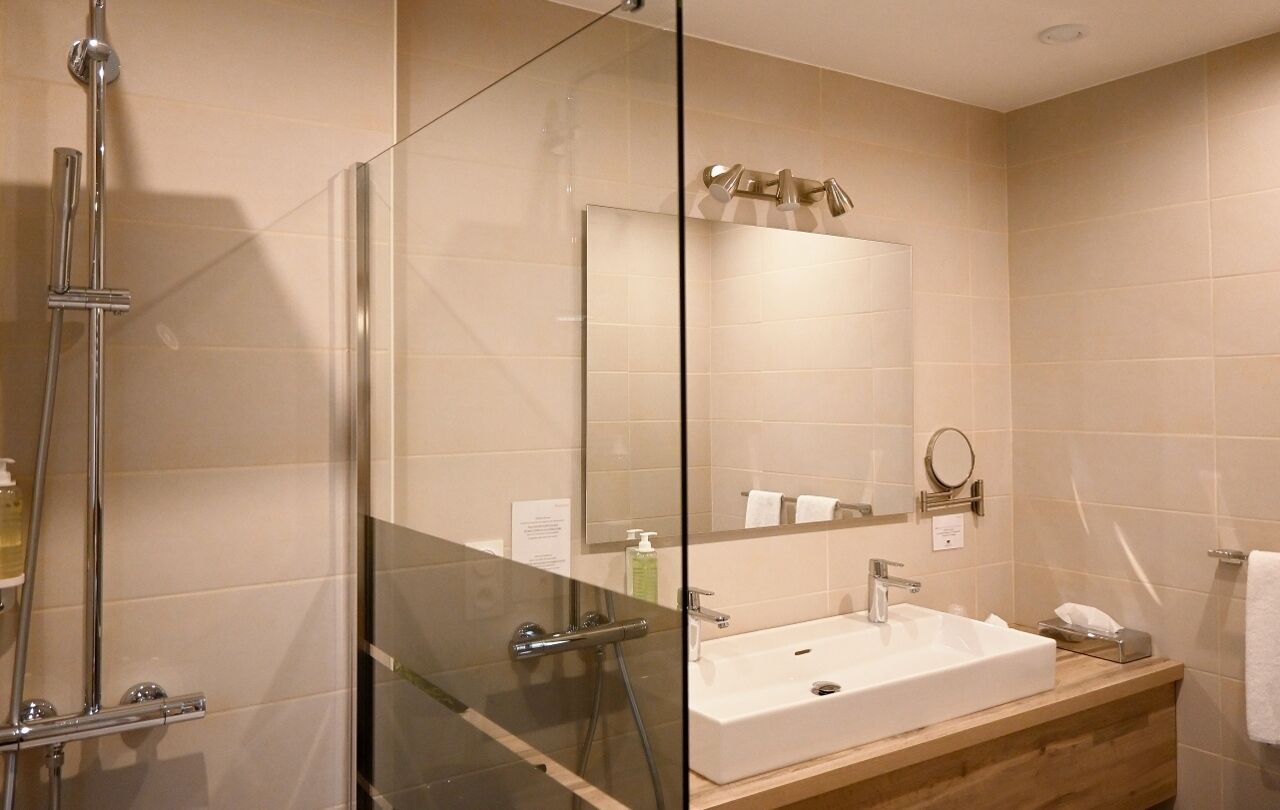 A modern bathroom with a glass-enclosed shower, a sink with a mirror, and beige tiled walls.