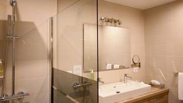 A modern bathroom with a glass-enclosed shower, a sink with a mirror, and beige tiled walls.