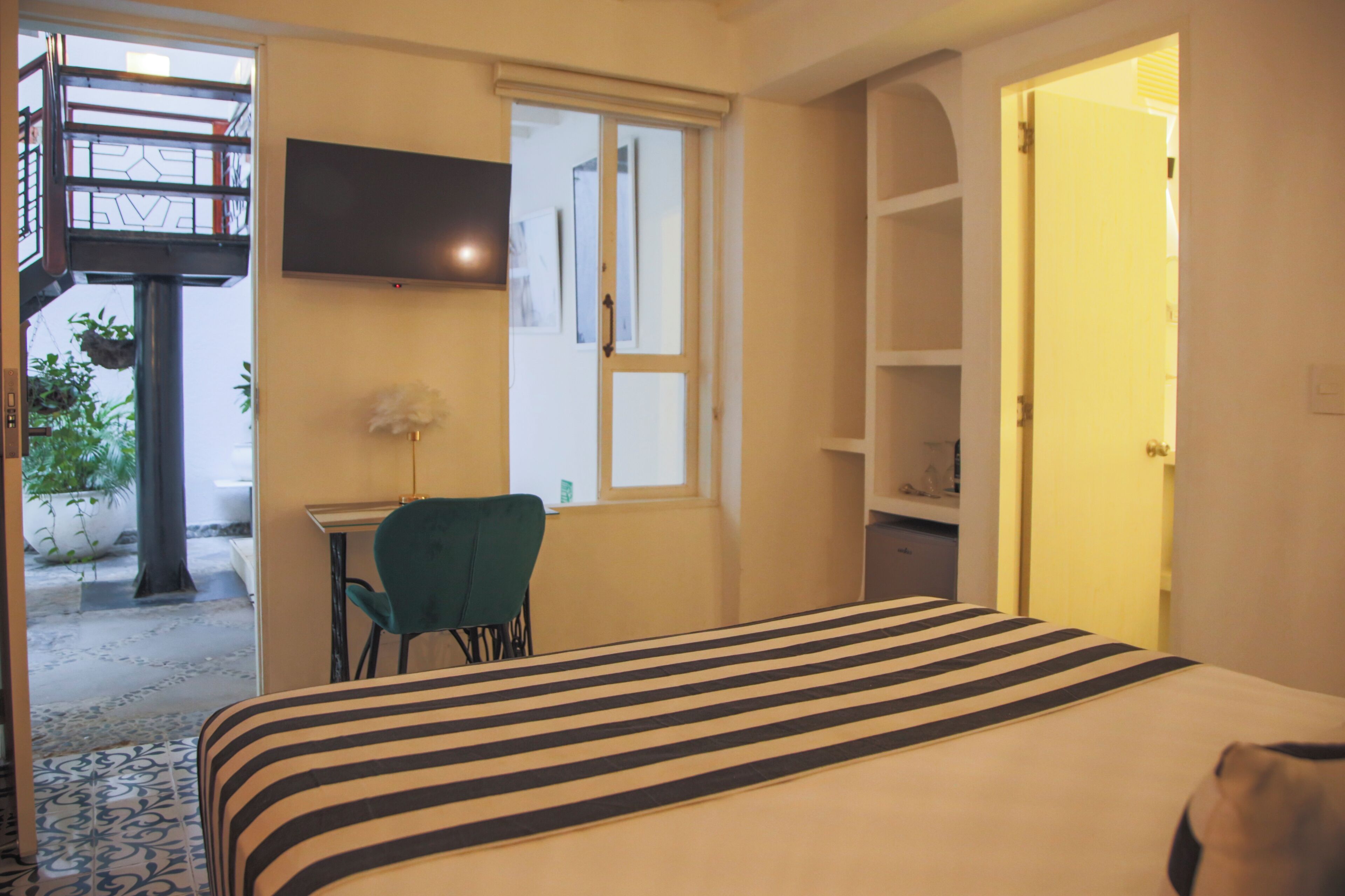 Een hotelkamer met een bed, een bureau met stoel, een aan de muur bevestigde televisie en een deur naar een andere kamer.