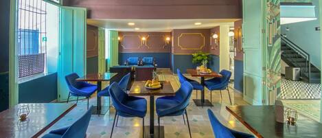 A restaurant with blue chairs, wooden tables, and a central dining table with fruit.