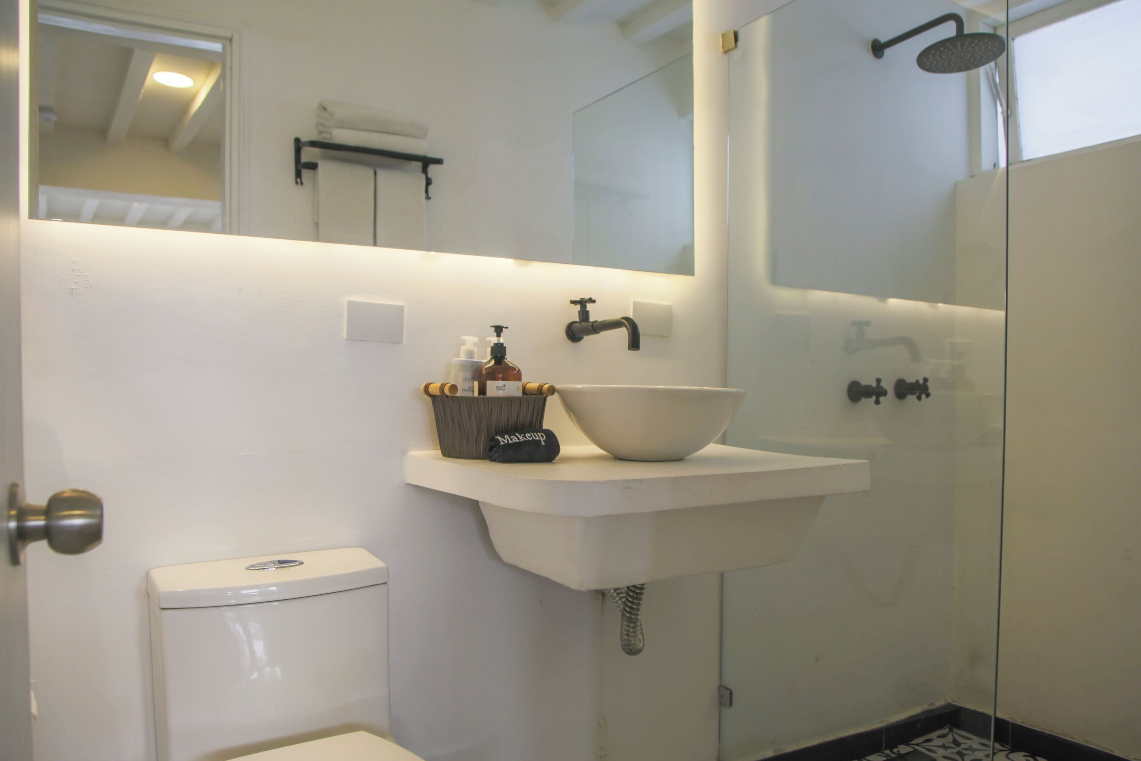 A bathroom with a white sink, a large mirror, a shower, and a toilet.