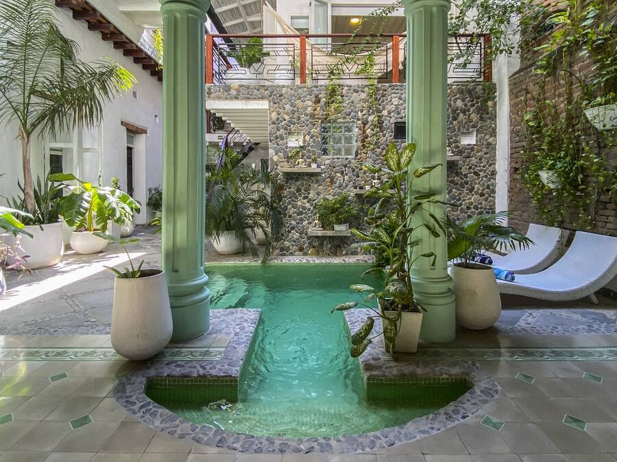 Un jardín interior tranquilo con una fuente central, paredes de piedra y plantas en macetas.