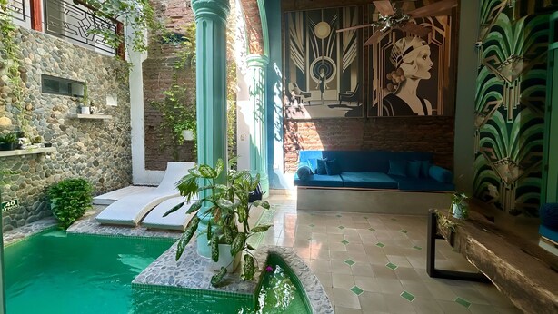 Un área de piscina con un muro de piedra, un sofá azul y un mural decorativo.