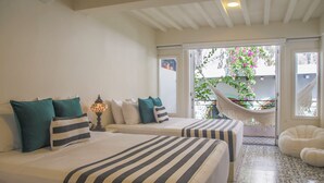 Habitación de hotel con dos camas, una hamaca, un balcón con plantas y una silla blanca.