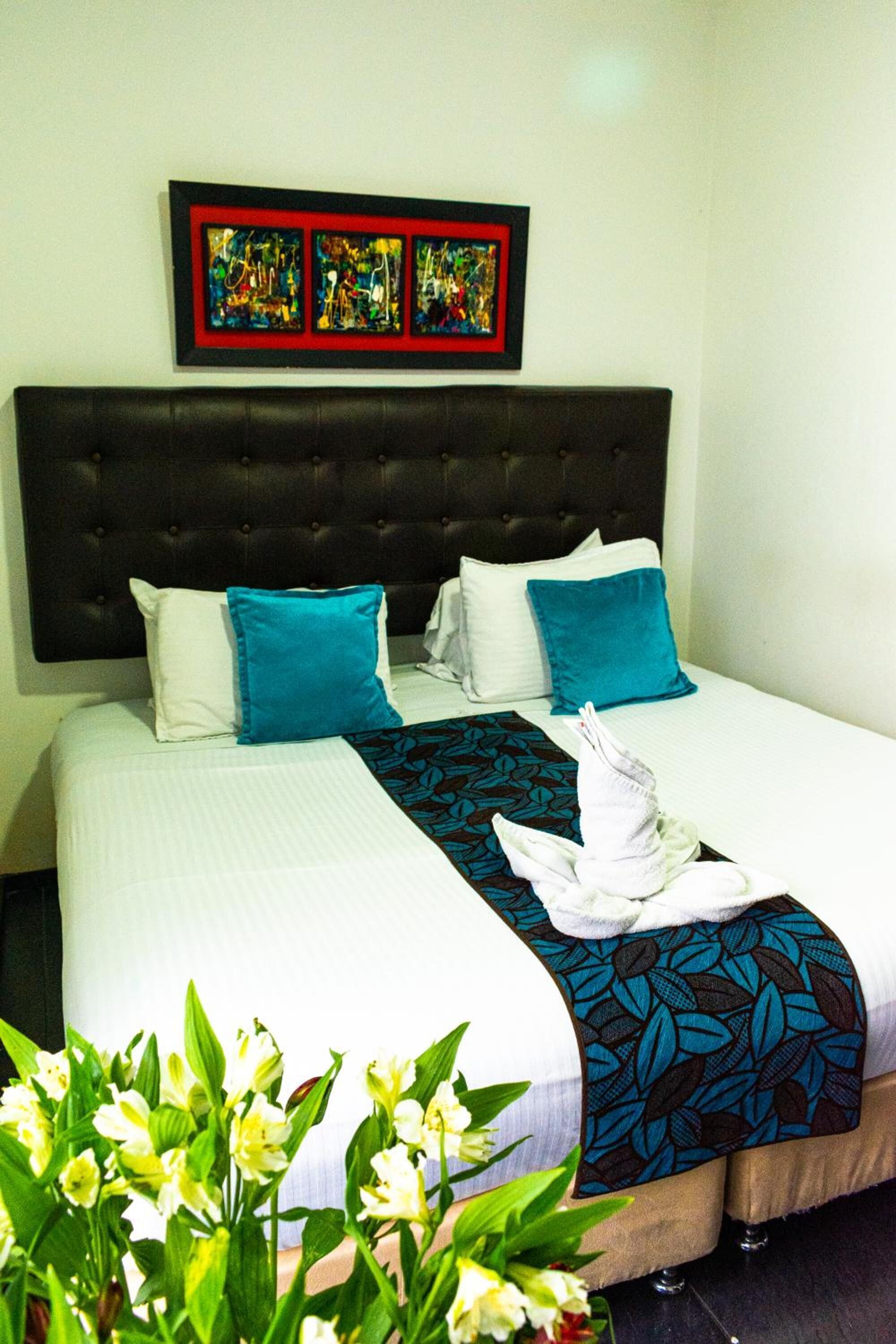 A neatly made bed with a headboard, white and blue pillows, a blue and black patterned throw, and a white towel folded on the bed.