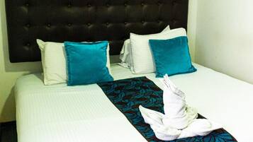 A neatly made bed with a headboard, white and blue pillows, a blue and black patterned throw, and a white towel folded on the bed.