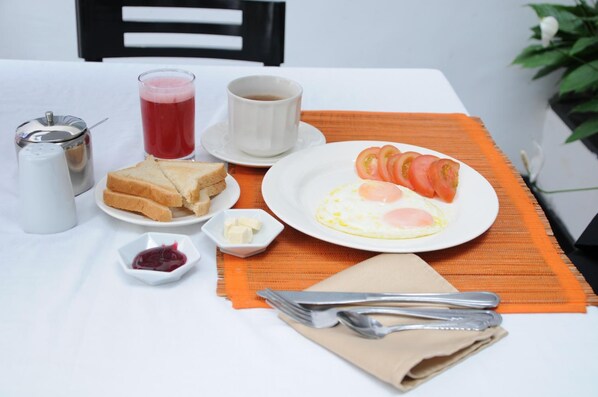 A breakfast setting with toast, eggs, tomatoes, jam, butter, a cup of coffee, and a jug of juice on a table with a placemat.