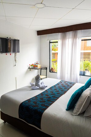 A hotel room with a bed, a television mounted on the wall, a small table with a plant, and a window with curtains. - Central House Hotel (Bogotá)