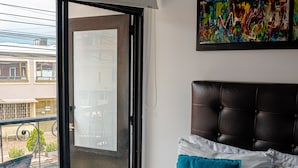Una habitación de hotel con cama, ventana con vistas al exterior, un cuadro en la pared y una toalla sobre la cama.