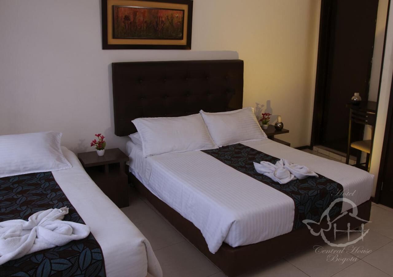 Una habitación de hotel con dos camas, un cabecero, una mesita de noche con un florero y un cuadro en la pared.