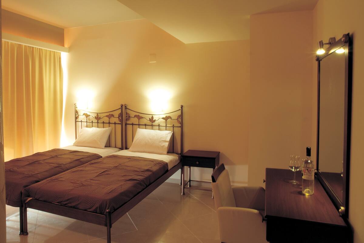 A bedroom with a large bed, bedside tables, a chair, a mirror, and a bottle of water.