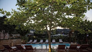 Área de piscina com espreguiçadeiras e uma árvore.