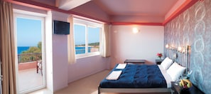 A bedroom with a bed, a TV, a nightstand, a vase with flowers, and a view of the sea.