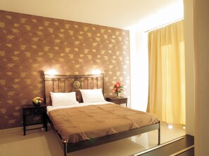A neatly made bed with a headboard, a bedside table with a vase of flowers, and a patterned wall.
