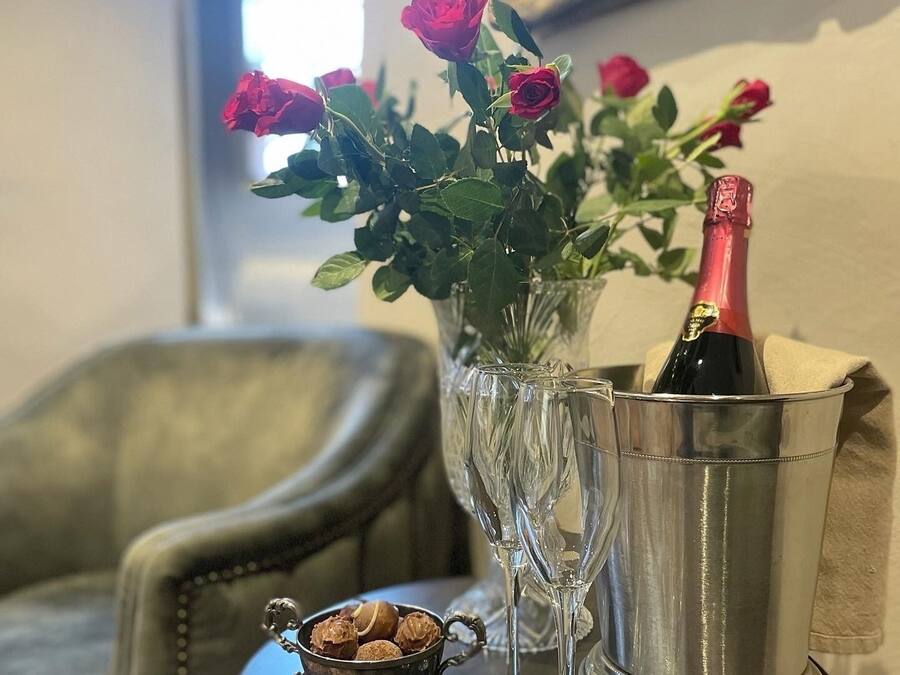 Ett bord med en vas med rosor, en flaska champagne och en liten skål med nötter.