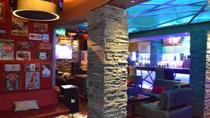 Zona de bar con pilares de piedra, asientos y una pared decorada con carteles antiguos.