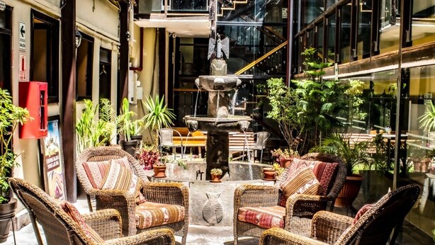 Un patio con sillas de mimbre, una fuente de piedra y plantas en macetas.