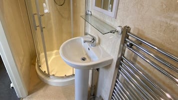 Un baño con cabina de ducha de vidrio, lavabo sobre pedestal, inodoro y perchero para toallas.