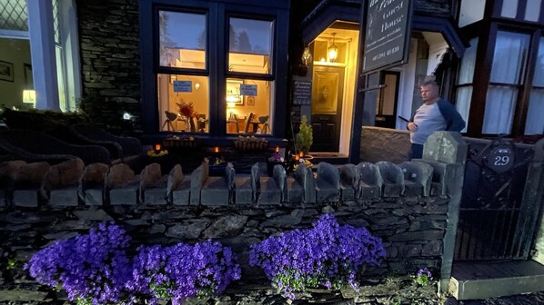 A stone wall with a row of sheep statues and purple flowers in front of a building with a sign reading "The Guest House".
