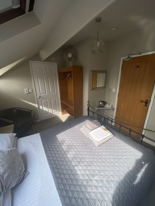 A bedroom with a bed, a wooden wardrobe, a mirror, a radiator, and a ceiling fan.