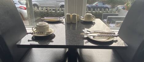 A dining area with a table set for two, chairs, and a view of parked cars outside.