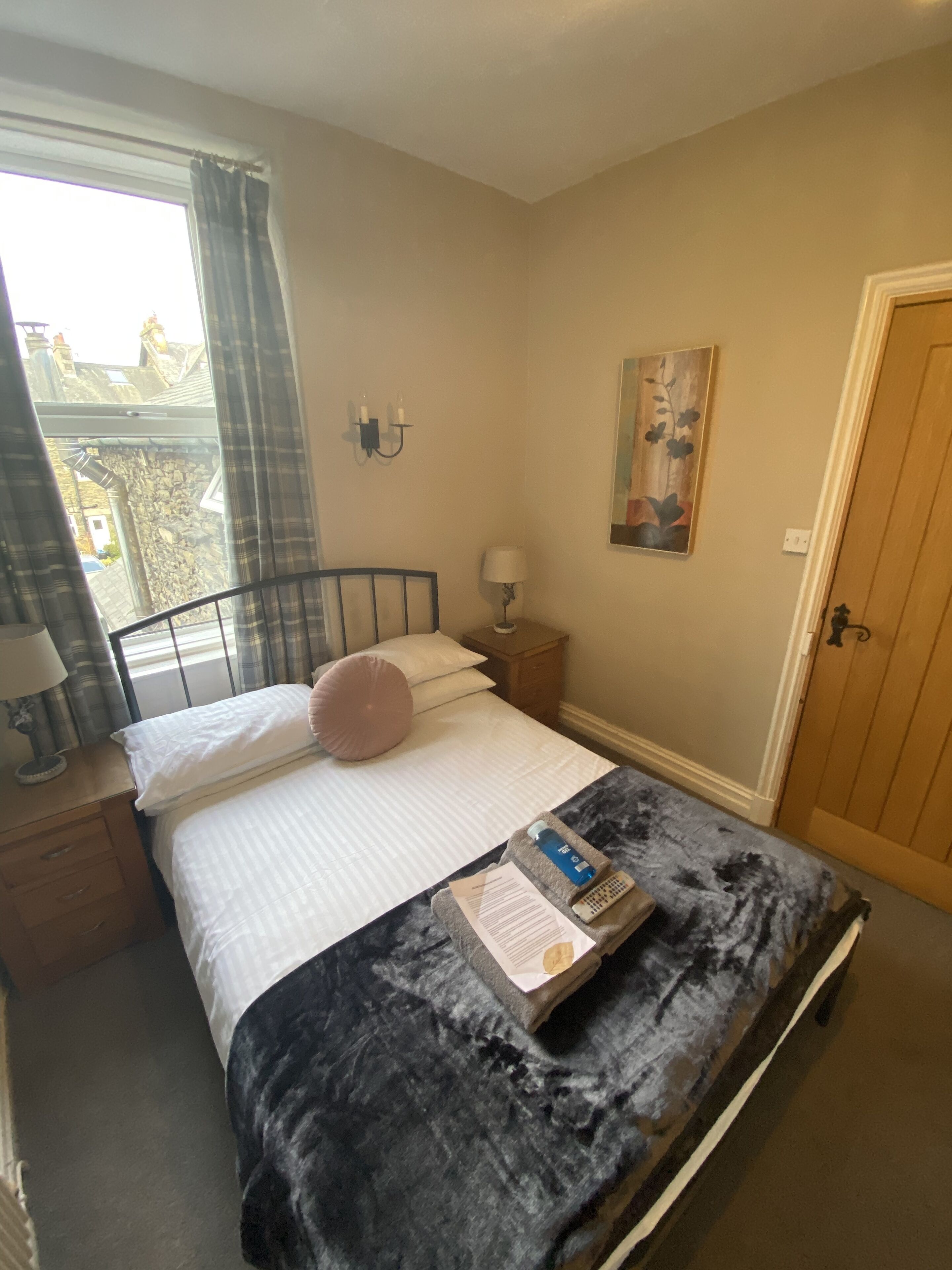 A bedroom with a bed, a nightstand, a lamp, a painting, and a door.