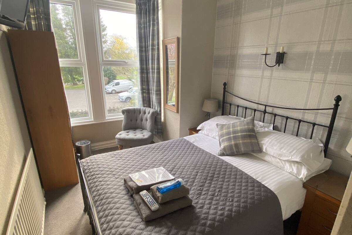 A neatly arranged bedroom with a large bed, a chair, a bedside table, and a window with curtains.