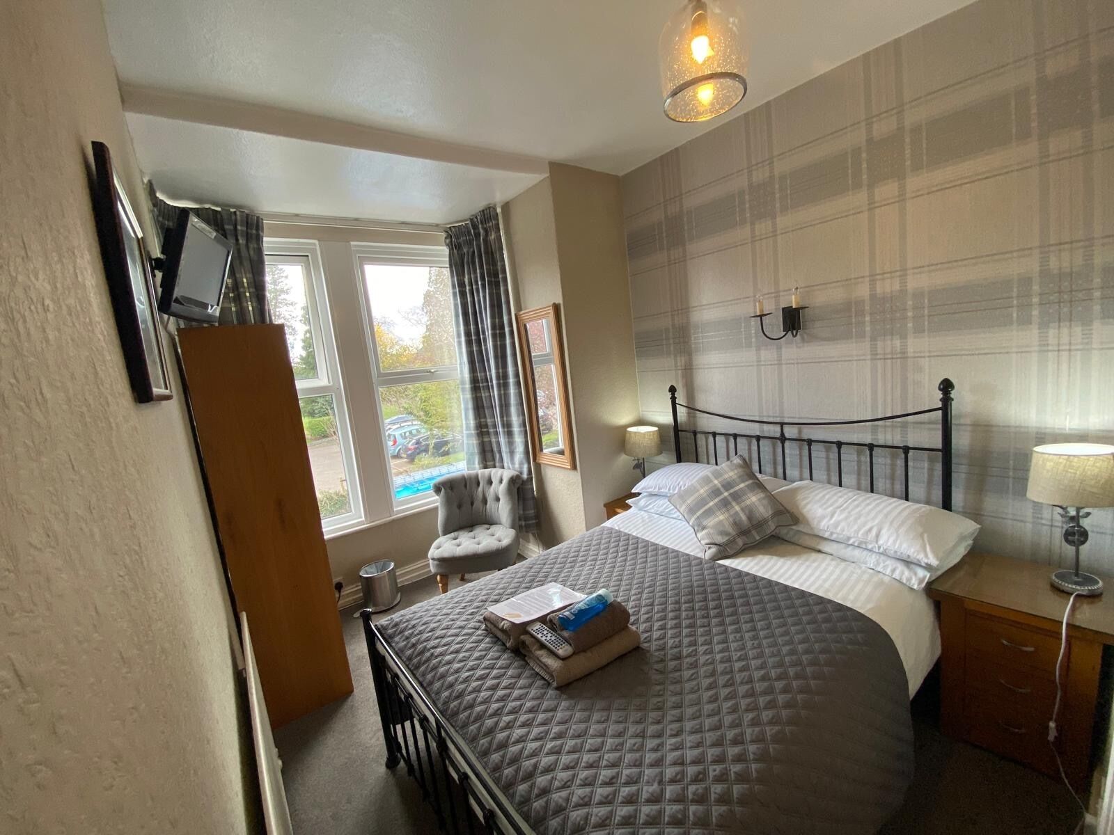 A bedroom with a bed, a chair, a desk, a window, and a wall-mounted lamp.