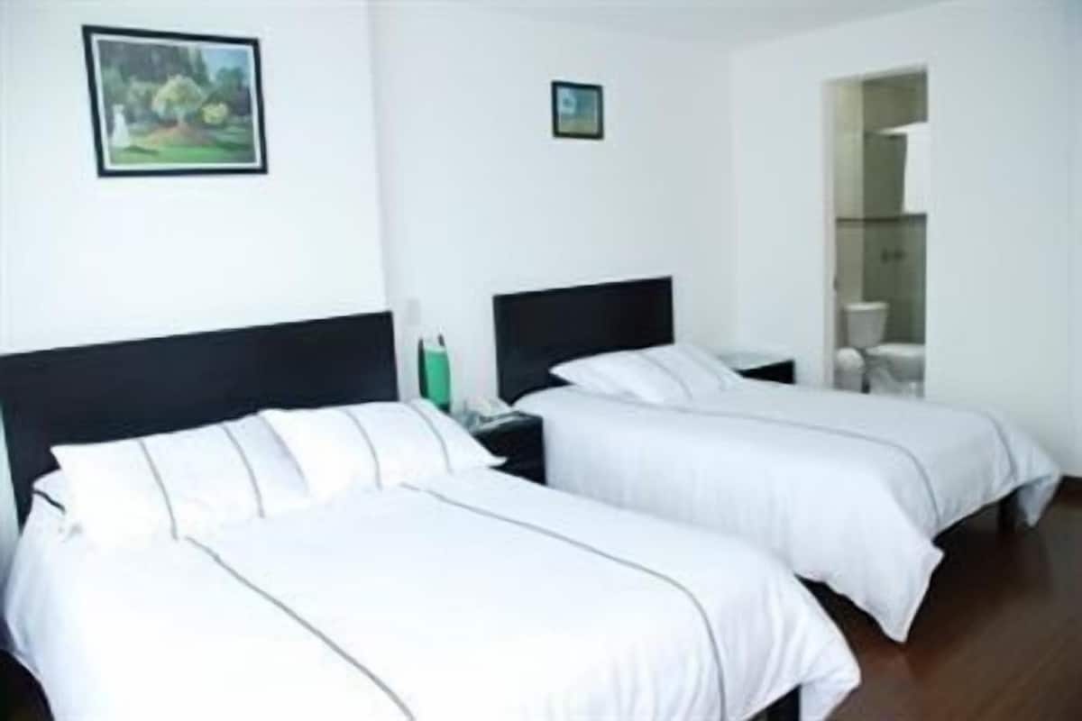 A hotel room with two single beds, a nightstand, a small table, and a framed picture on the wall.