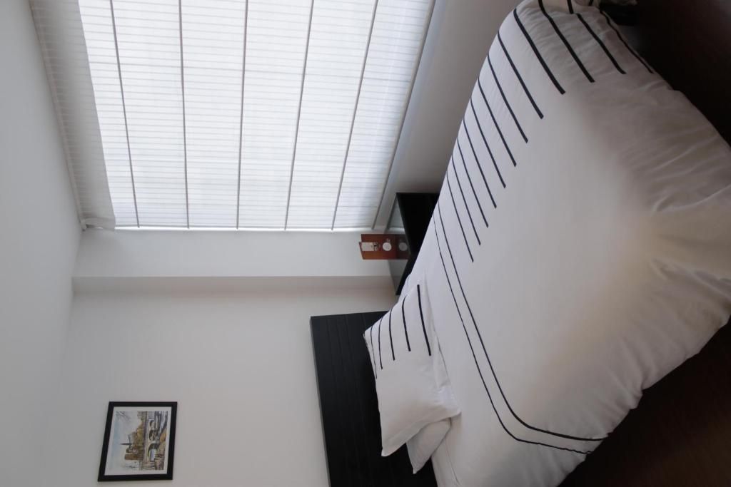 A room with a bed, a window with blinds, a framed picture on the wall, and a small table with a decorative item.