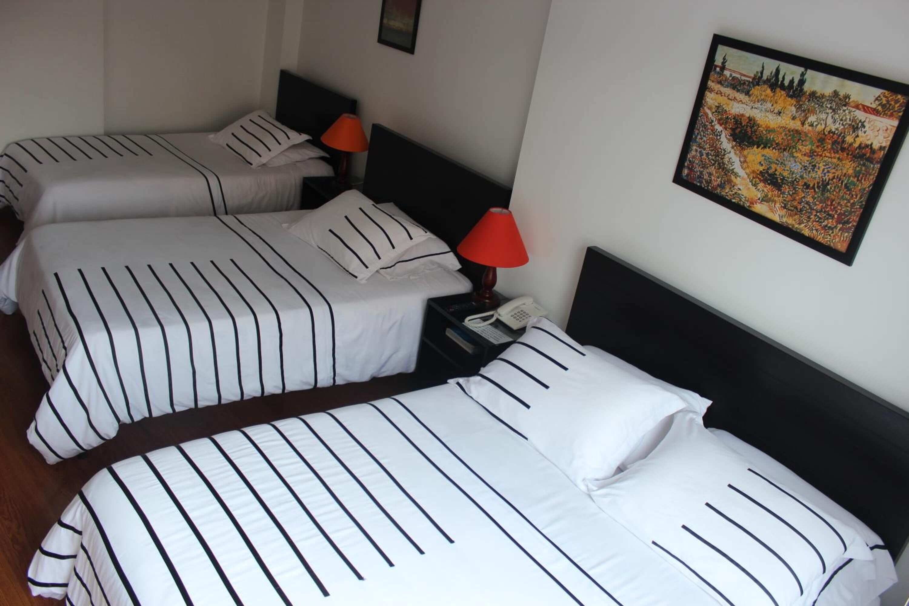 Een hotelkamer met twee bedden, elk met gestreepte lakens en een rode lamp op het nachtkastje.