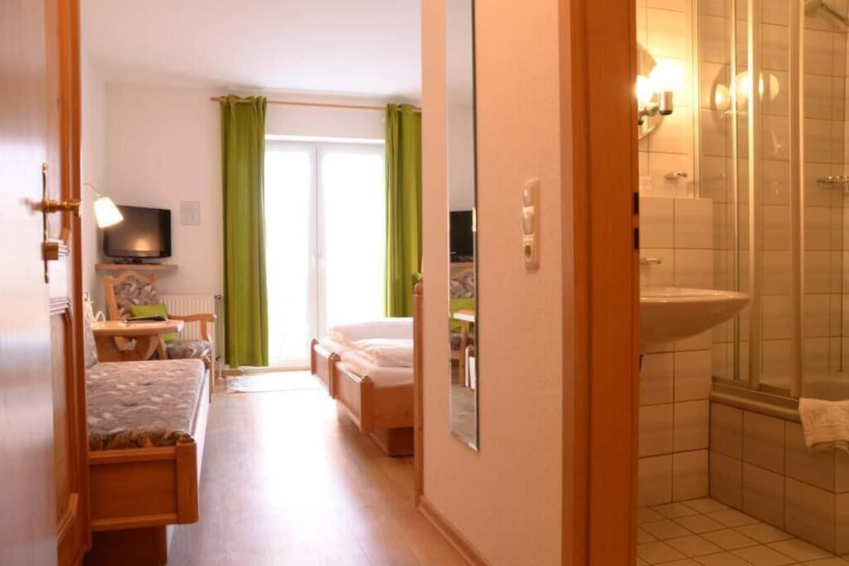 Un dormitorio con cama, mesita de noche, televisor y ventana con cortinas verdes.