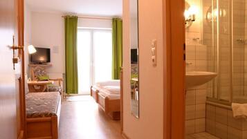 Un dormitorio con cama, mesita de noche, televisor y ventana con cortinas verdes.