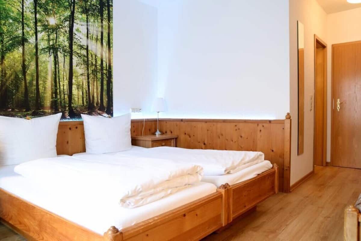 Un dormitorio con cama de madera, mesita de noche, lámpara de pared y una puerta.