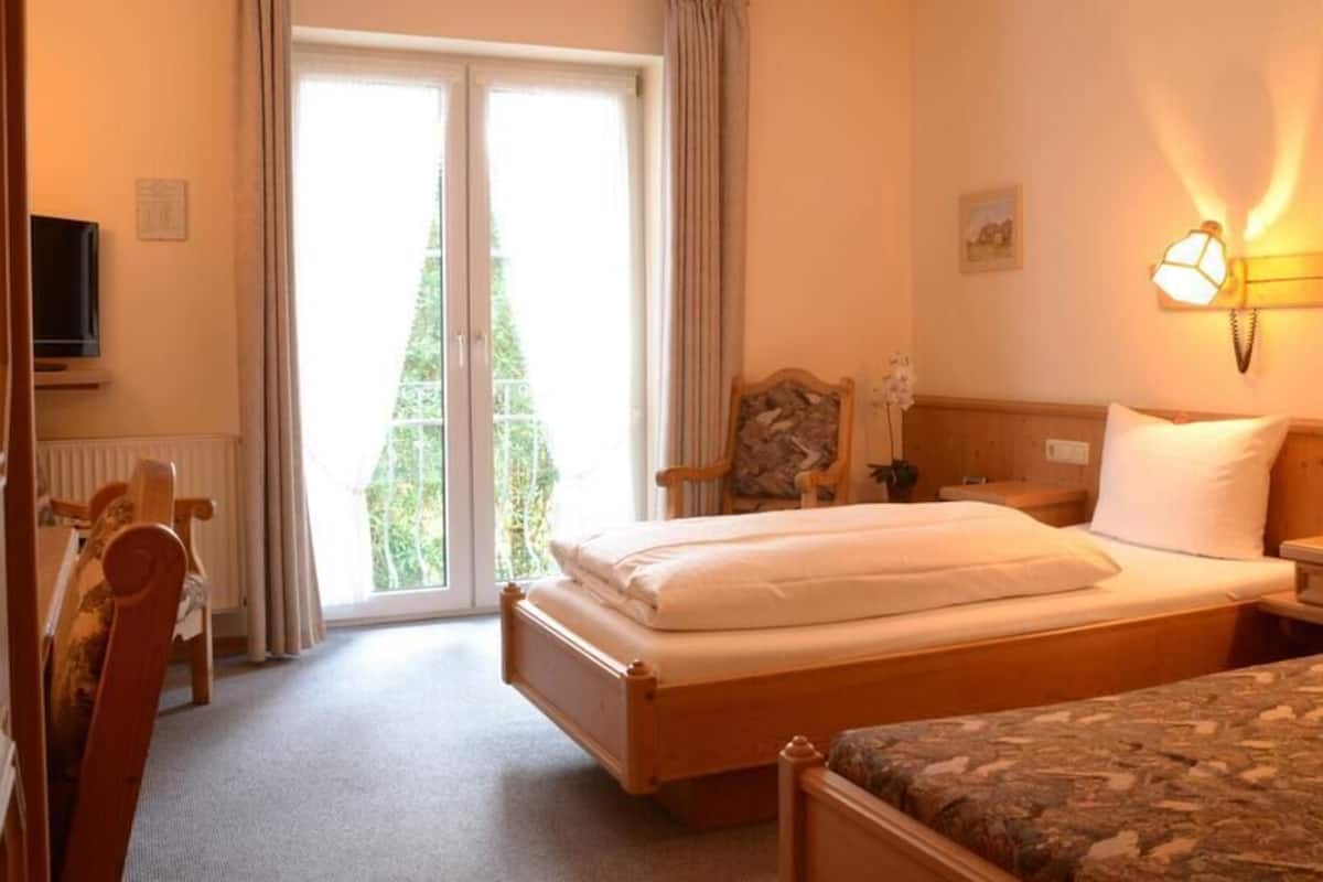 Habitación de hotel con cama doble, una silla, escritorio, televisor y vistas al exterior a través de una puerta corredera.