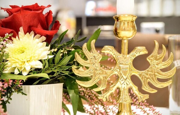 A decorative arrangement with a golden candelabra, red and white flowers, and green foliage. - Waldhotel Twiehaus (Lübeck)