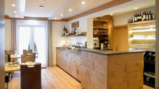 Une cuisine moderne avec des meubles en bois, un îlot central et un coin bar agrémenté de bouteilles de vin et de verres.