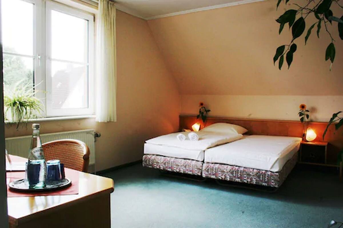 A bedroom with a bed, bedside lamps, a window, a chair, and a table with a bottle.