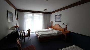 Habitación de hotel con cama doble, un escritorio con silla, una mesita con lámpara y una ventana con cortinas.